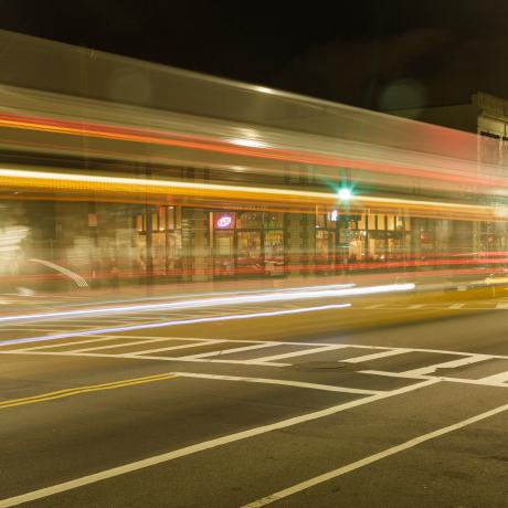 A street-view that it well-lit at night-time with driving cars out of focus 