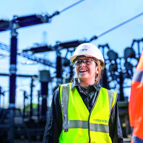 National Grid worker with an out of focus industrial site in the background under a blue sky