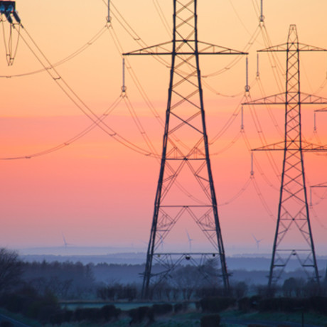 Row of lattice electricity pylons against an orange sky