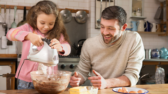 Young girl whisking birthday cake mix with father in the kitchen