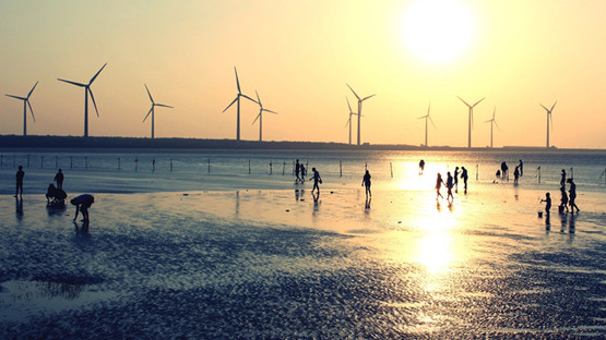 Silhouettes of people on a beach at sunset with wind turbines out at sea in the background