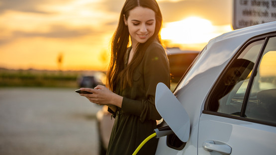 Person holding a mobile device leaning against electric vehicle while it's charging