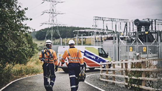 Two engineers wearing PPE walking towards a National Grid van parked outside an electricity transmission substation