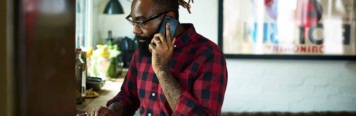 Bearded man with tattoos using laptop while talking on mobile phone in design studio